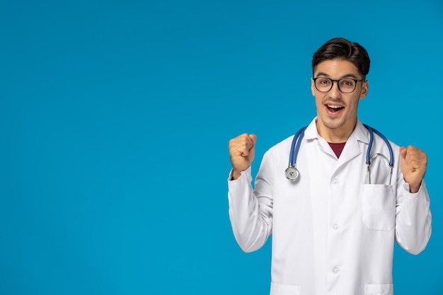 Doctors day handsome brunette cute guy in medical gown happy holding fists up