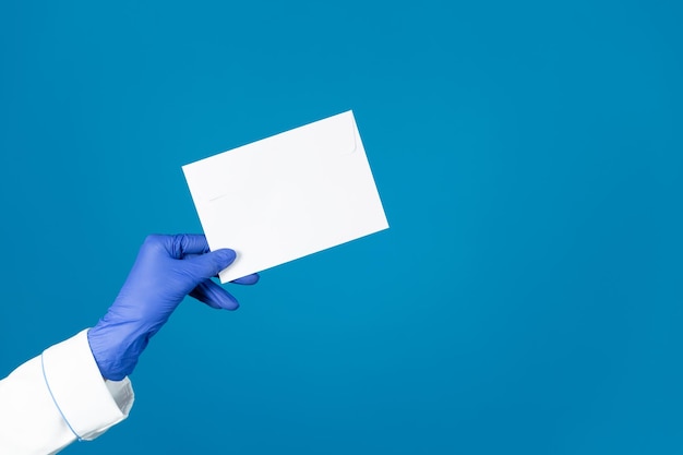 Doctors hand in a glove holds an envelope on a blue background with copy space.