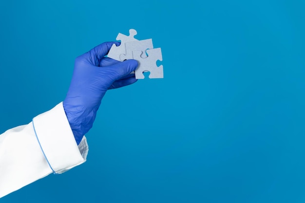 Doctors hand in a glove holds a puzzles on a blue background with copy space