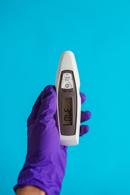 a doctors hand wearing a purple glove holding a thermometer on blue background