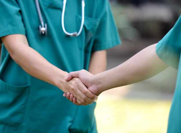 Doctors in a medical team handshake together outdoor on the green park background (volunteer)