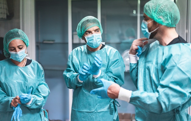 Doctors and nurse preparing to work in hospital for surgical operation during coronavirus pandemic outbreak - Medical workers getting dressed inside clinic