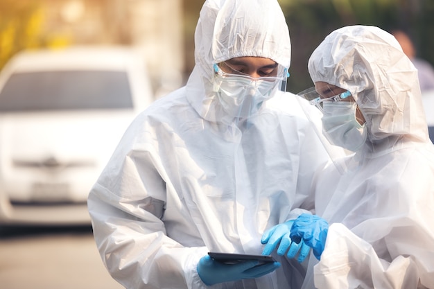 Doctors in ppe suit using tablet with face shield discussing standing on street