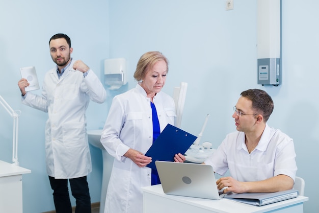 doctors using a laptop, discussing diagnosis while standing in clinic