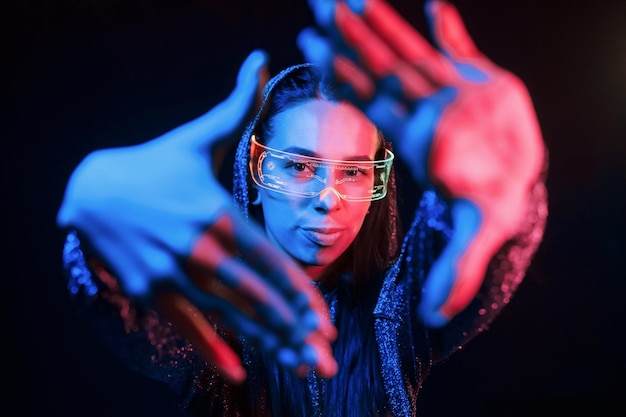 Does gestures by hands Portrait of young girl that is in eyeglasses in blue neon lighting