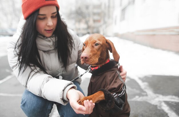 Dog in the clothes and the girl are sitting on the winter street