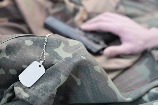 Dog tags lies with hand of depressive man who commit suicide with a gun. Concept of veteran who can no longer stand the pain decides to kill himself.