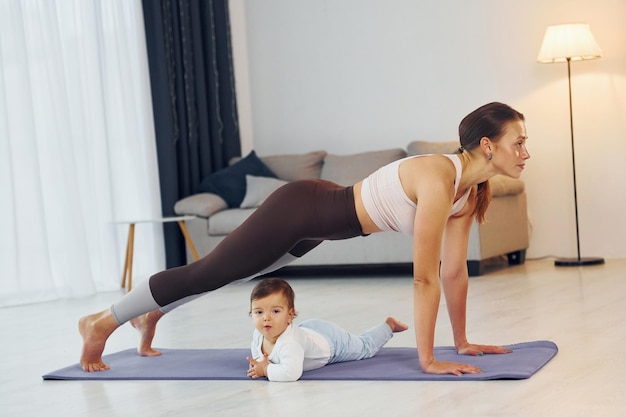 Doing exercises on the mat Mother with her little daughter is at home together