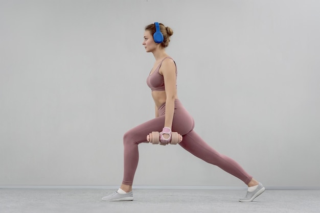 Doing step split stretch athletic young woman use heavy lifting using dumbbell at the gym