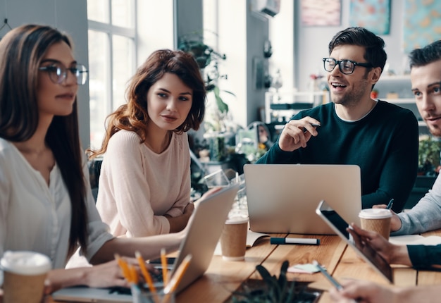 Doing what the love. Group of young modern people in smart casual wear discussing something and smiling while working in the creative office