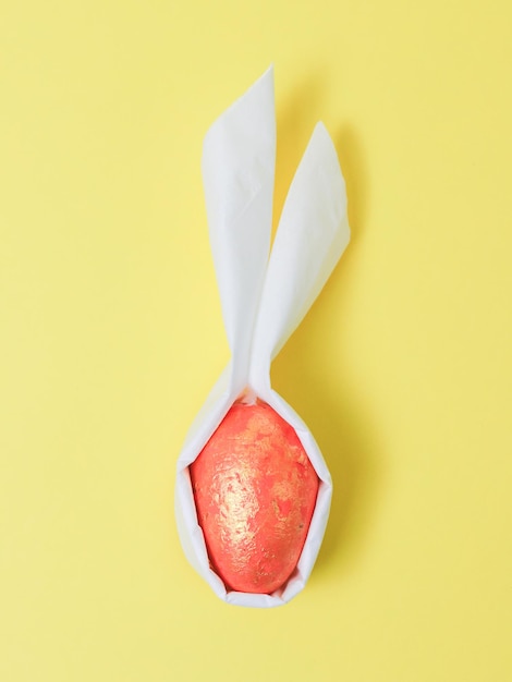 A doityourself decorative orange marble egg with white paper ears on a yellow background