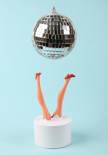 Doll feet and disco ball on a blue background Minimalistic party concept