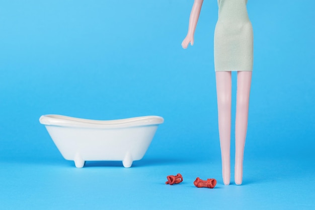 Doll girl in a dress with shoes removed on the background of a bath on a blue background