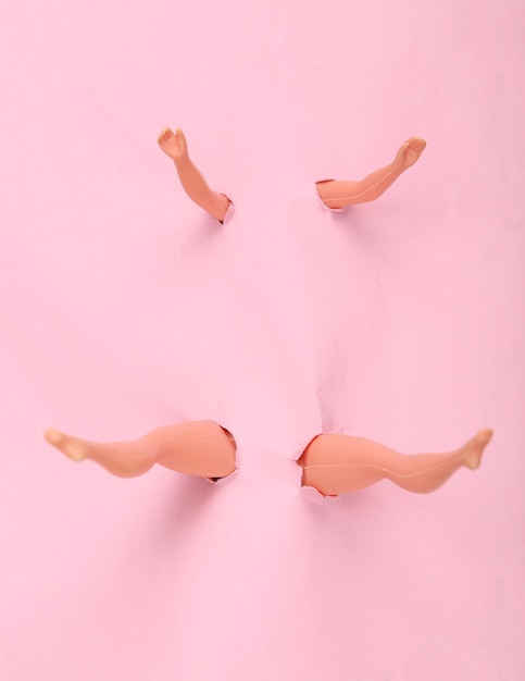 Doll legs and arms through the torn hole of pink paper Minimalism concept art