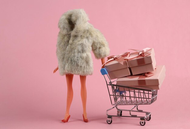 Doll mannequin in warm fur coat and shopping trolley with gift boxes on pink background Minimalism holiday concept Concept art