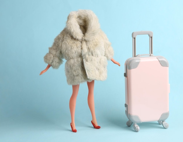 Doll mannequin in warm fur coat with luggage on blue background Minimalism fashion shot Concept art