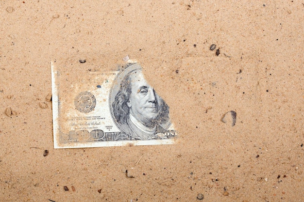 A dollar bill is laying on the sand.