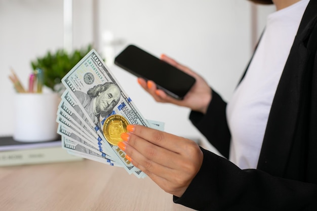 Dollar bills and dogecoin at woman hands with phone in workplace