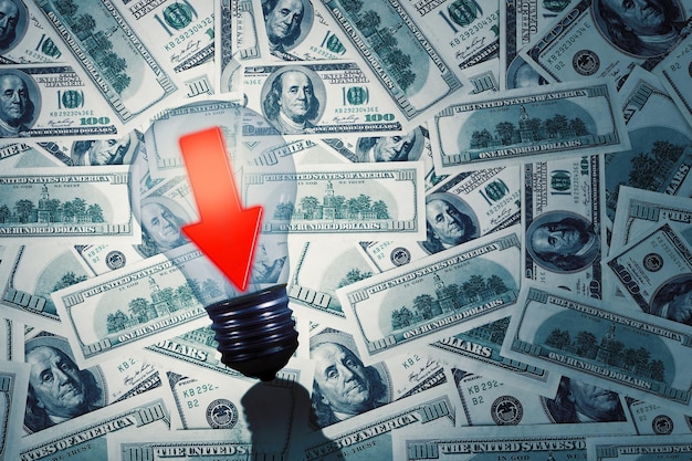 Dollar bills with downwards arrow in a light bulb