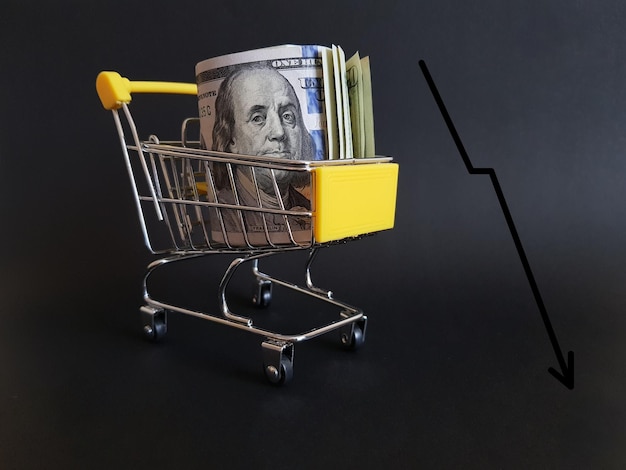 Dollars in a cart on a black isolated background with a falling graph