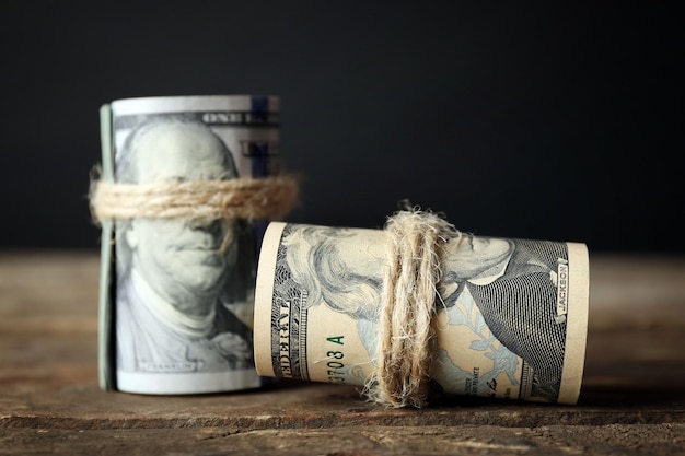 Dollars roll on wooden table in front of dark background