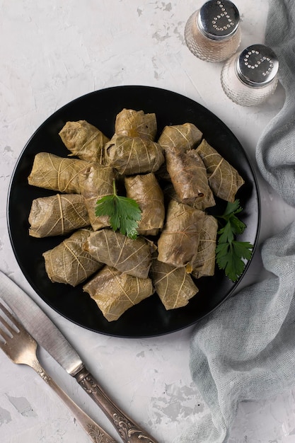 Dolma  stuffed grape leaves with rice and meat on black plate on light gray background