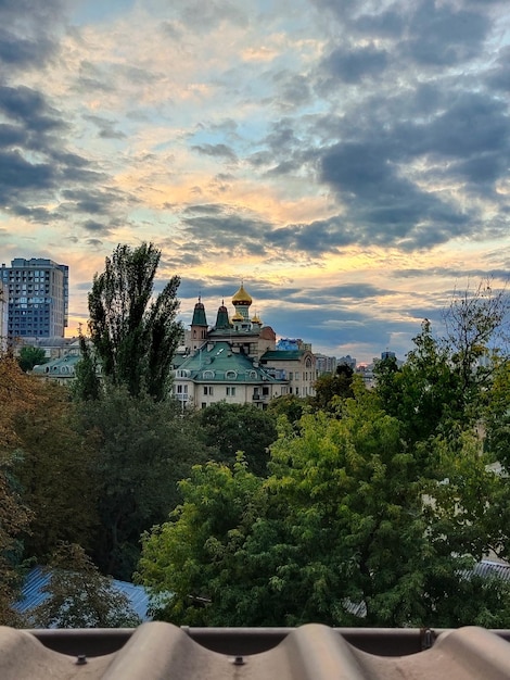 The domes of the Christian church can be seen above the green trees in the park against the cloudy sky