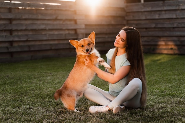 Domestic Corgi dog with girl owner Young woman sitting on the grass and hug Welsh Corgi Pembroke Lifestyle with domestic playful dog