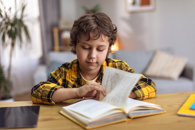 Domestic learning Cute little boy study to read reading book at desk studying at home free space