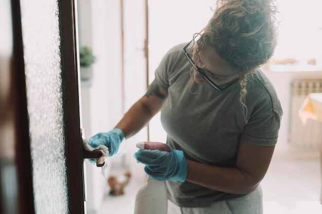 Domestic work at home One woman cleaning door in apartment with spray and gloves Housewife job Hygiene and sanitize life place Housemaid working and clean house surfaces Concept of healthy