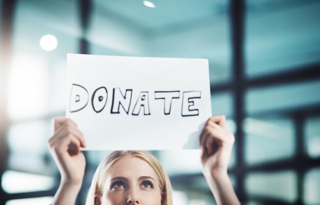 Photo donate volunteer and give back to the community with a sign in the hands of a young woman inside closeup of a poster with text looking for welfare aid donations and contributions to society