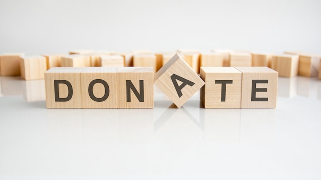 DONATE - word of wooden blocks with letters on a gray background. Reflection of the caption on the mirrored surface of the table. Selective focus.