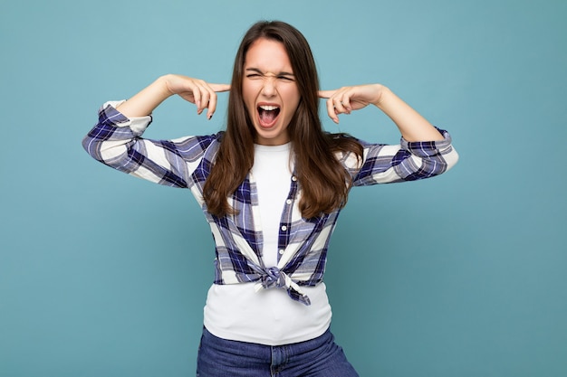 Dont want to hear it young emotional attractive brunette woman wearing check shirt isolated on blue