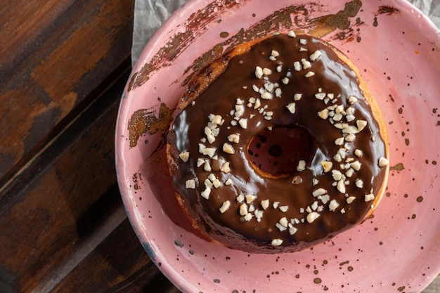 Donut sprinkled with chocolate icing and sprinkled with chopped nuts It lies on designer pink plate