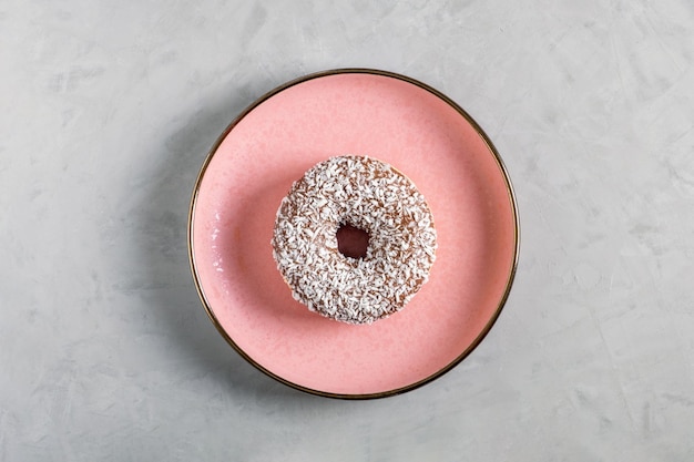 Donut with coconut topping lies on a pink ceramic plate on a gray background View from above Selective focus