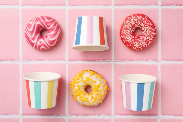 Donuts on a pink tile with paper cups