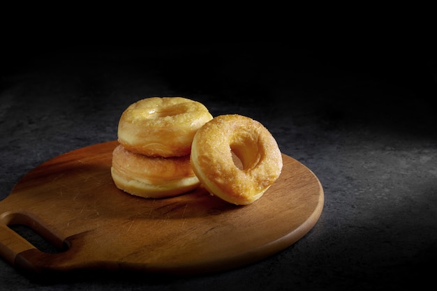 Donuts with sugar on a wooden plate over a dark table background.