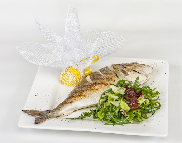 Dorada fish with salad on the white plate Studio shot