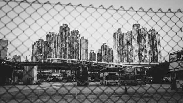 Photo double-decker buses in station by modern building seen through chainlink fence