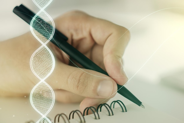 Double exposure of creative DNA hologram and man hand writing in notebook on background Bio Engineering and DNA Research concept