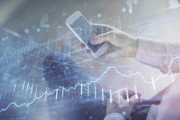 Double exposure of man's hands holding and using a digital device and forex graph drawing Financial market concept