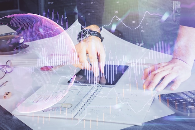 Double exposure of man's hands holding and using a digital device and forex graph drawing Financial market concept