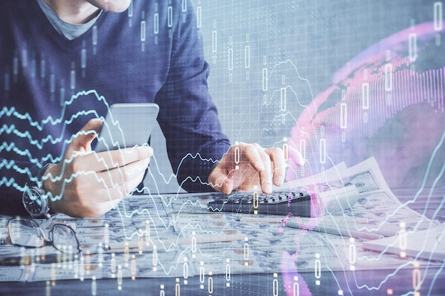 Double exposure of man's hands holding and using a digital device and forex graph drawing Financial market concept