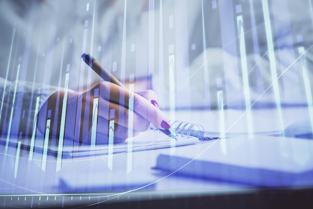 Double exposure of woman's hands making notes with forex graph hologram Concept stock market analysis