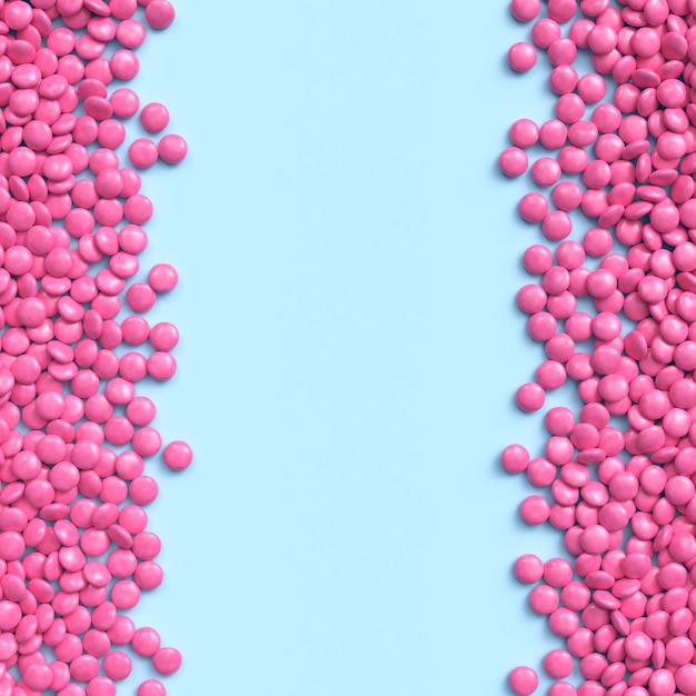 Double vertical border of pink coated chocolate candies on blue pastel background