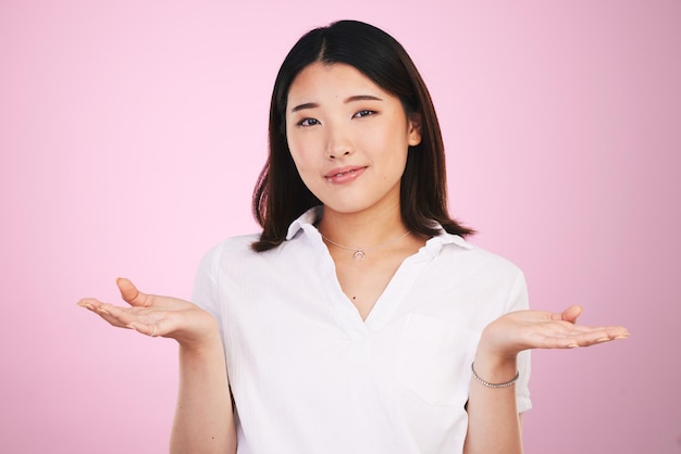 Doubt decision and portrait of Asian woman on pink background for unsure uncertainty and question Thinking confused and face of person with hand gesture for option choice and emoji in studio