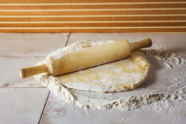 Dough is rolled out on the table. Nearby is a rolling pin. The table is sprinkled with flour.