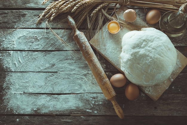 Dough, rolling pin and wheat ears on the old wooden background floured