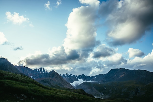 Photo dramatic alpine landscape with mountain ridge under cloudy sky. large cloud in blue sky above silhouettes of mountain range. big cloud in gradient sky above mountains silhouettes and beautiful glacier