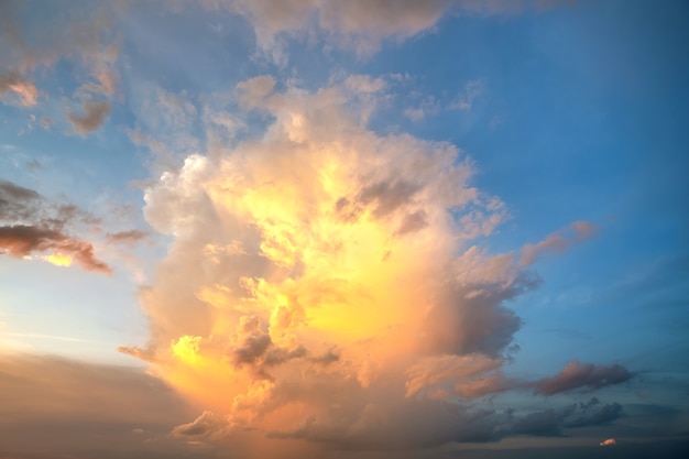 Dramatic cloudscape with puffy clouds lit by orange setting sun and blue sky.